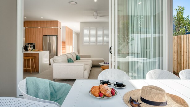 Ein modernes Wohnzimmer mit Esstisch für zwei Personen, einer Couch und einer Küche im Hintergrund.
