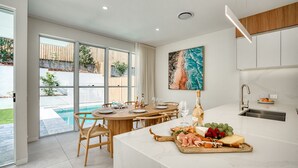 Eine moderne Küche mit Marmorarbeitsplatte, ein Essbereich mit rundem Tisch und Blick auf einen Swimmingpool.