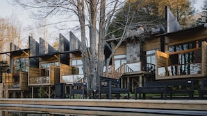 A modern wooden cabin with multiple levels and large windows, situated beside a reflective pool. - Ni-Newen (Pucón)