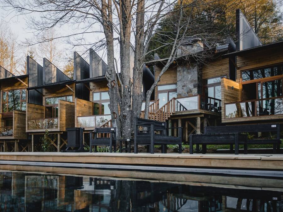 A modern wooden cabin with multiple levels and large windows, situated beside a reflective pool.