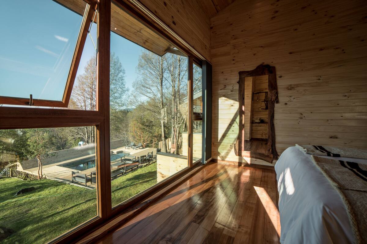 A room with large windows, wooden floors, and a bed with a striped blanket.