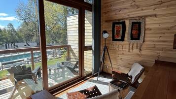 A wooden cabin with large windows, a deck, and a cozy seating area with a piano.