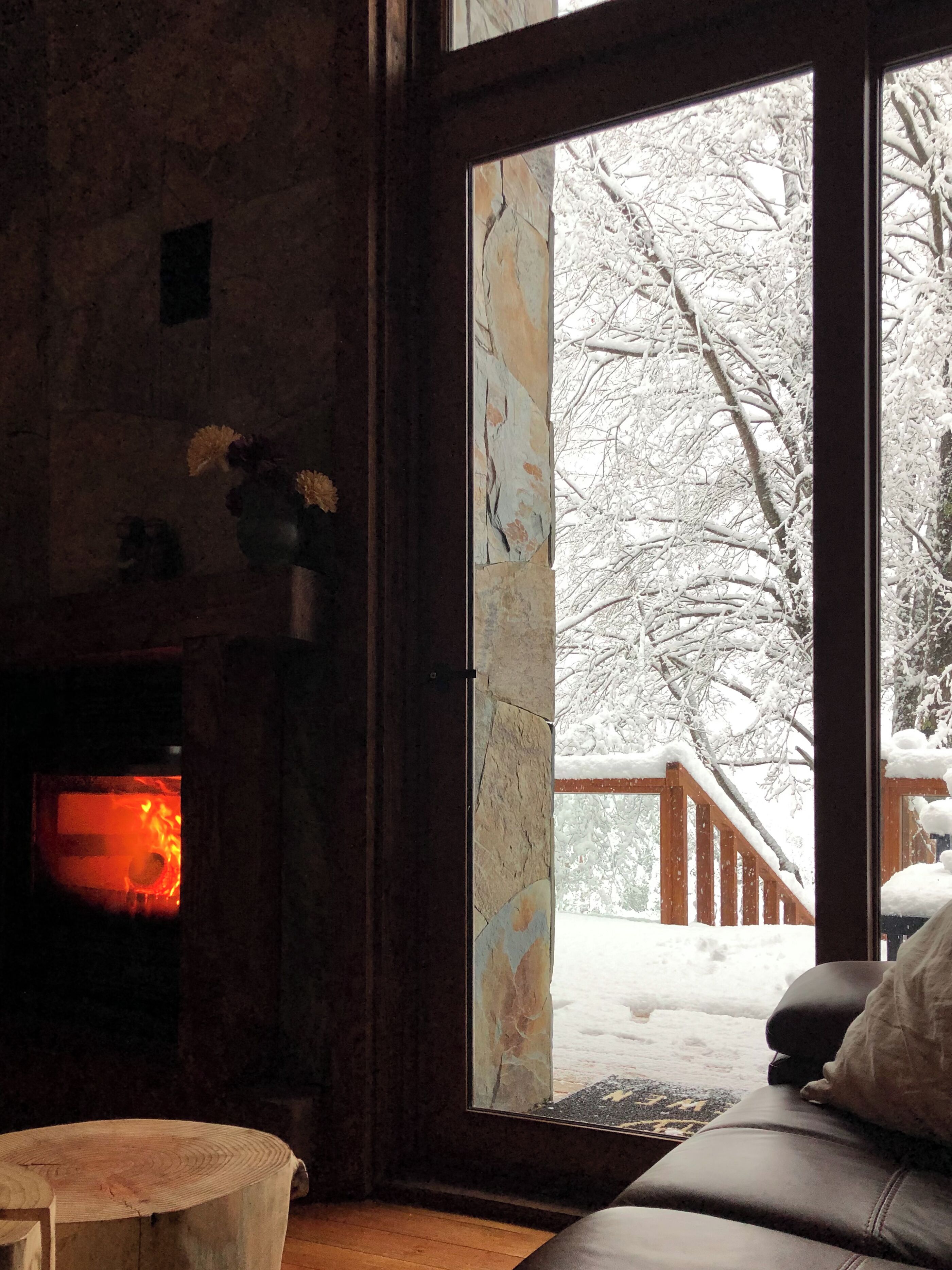 Een gezellige kamer met een open haard, een houten bank en uitzicht op een besneeuwde veranda.