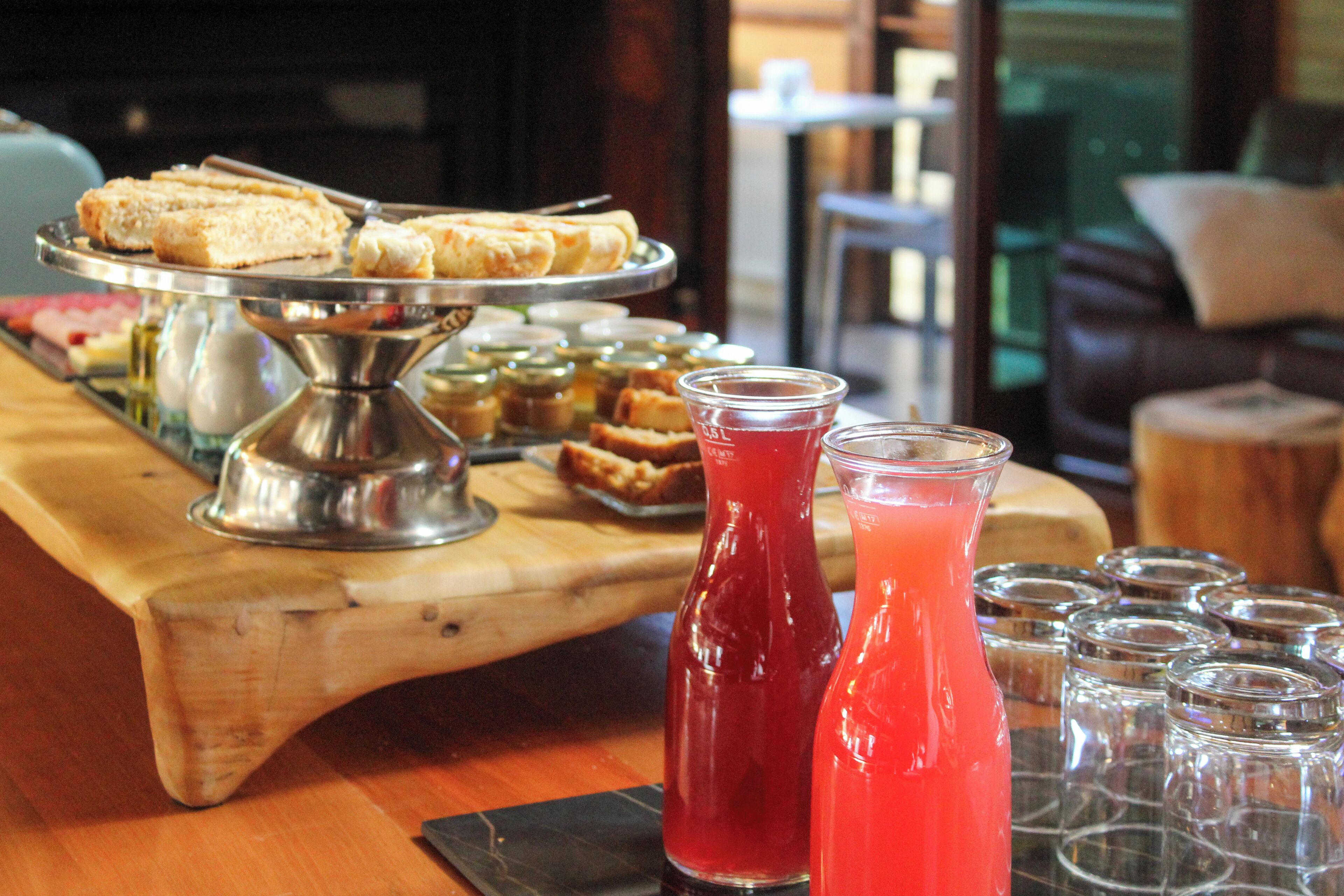 A buffet table with sandwiches, a drink dispenser, and several empty glasses.