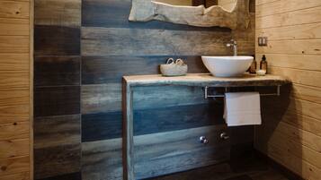 A modern bathroom with a wooden floor, a large mirror, a vessel sink, and a wooden vanity.