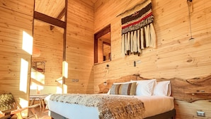 A wooden cabin interior with a bed, wooden floors, a ceiling fan, and a wall with hanging items. - Ni-Newen (Pucón)