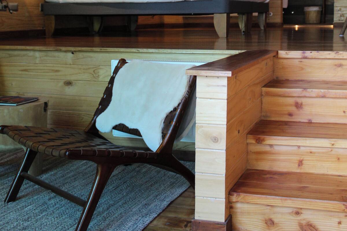A wooden cabin interior with a bed, a chair, and a small table.
