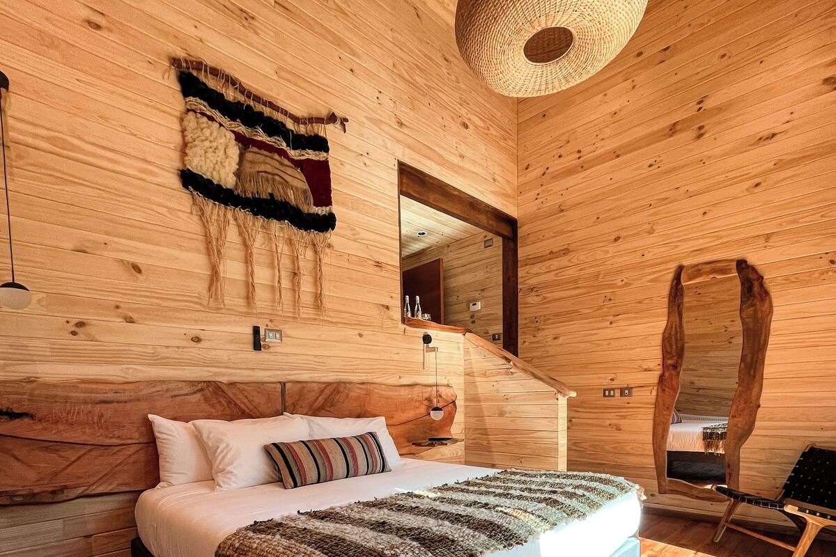 A wooden cabin-style bedroom with a bed, a hanging light fixture, and a mirror.