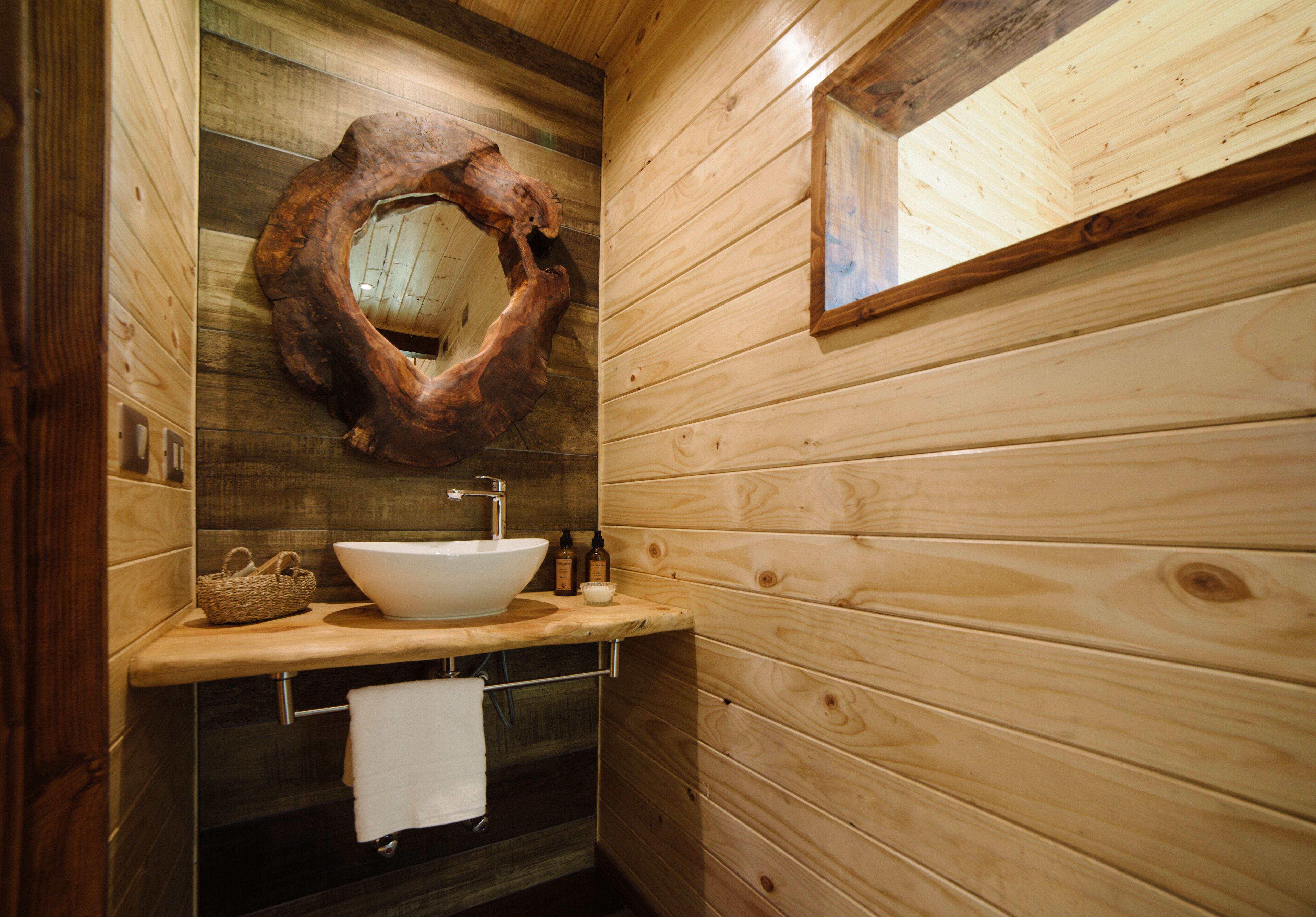 A wooden cabin bathroom with a large wooden sink, a mirror, and a towel rack.