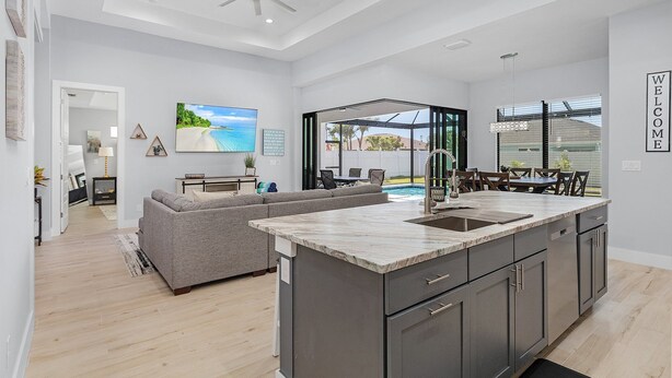 Una cucina moderna con una grande isola, una zona pranzo con vista piscina e un soggiorno con divano grigio.