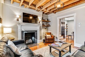 A living room with a fireplace, leather sofa, wooden coffee table, and a dining area with a chair and table.