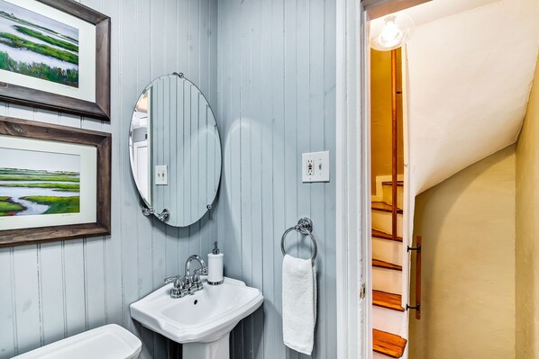 Un baño con lavamanos, espejo y dos cuadros enmarcados con paisajes.