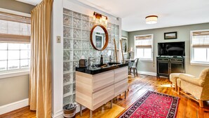 A modern bathroom with a glass backsplash, a wooden vanity, a round mirror, and a black countertop.