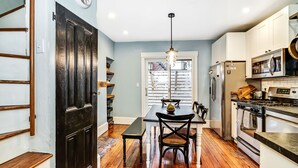 A kitchen with wooden flooring, a dining table with chairs, a refrigerator, an oven, and a microwave.