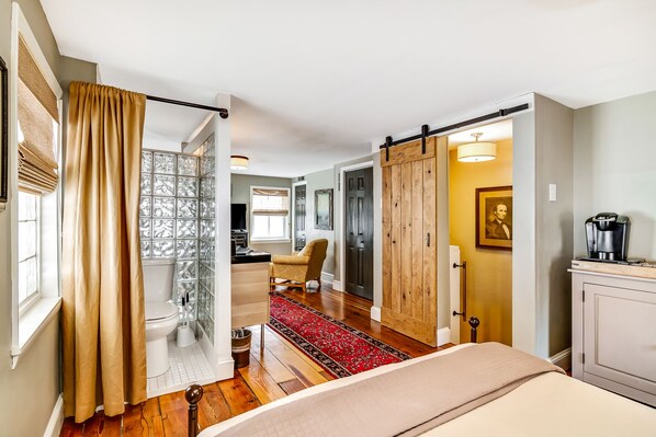 A hotel room with a large bed, a wooden wardrobe, a red carpet, and a bathroom with a glass shower enclosure.