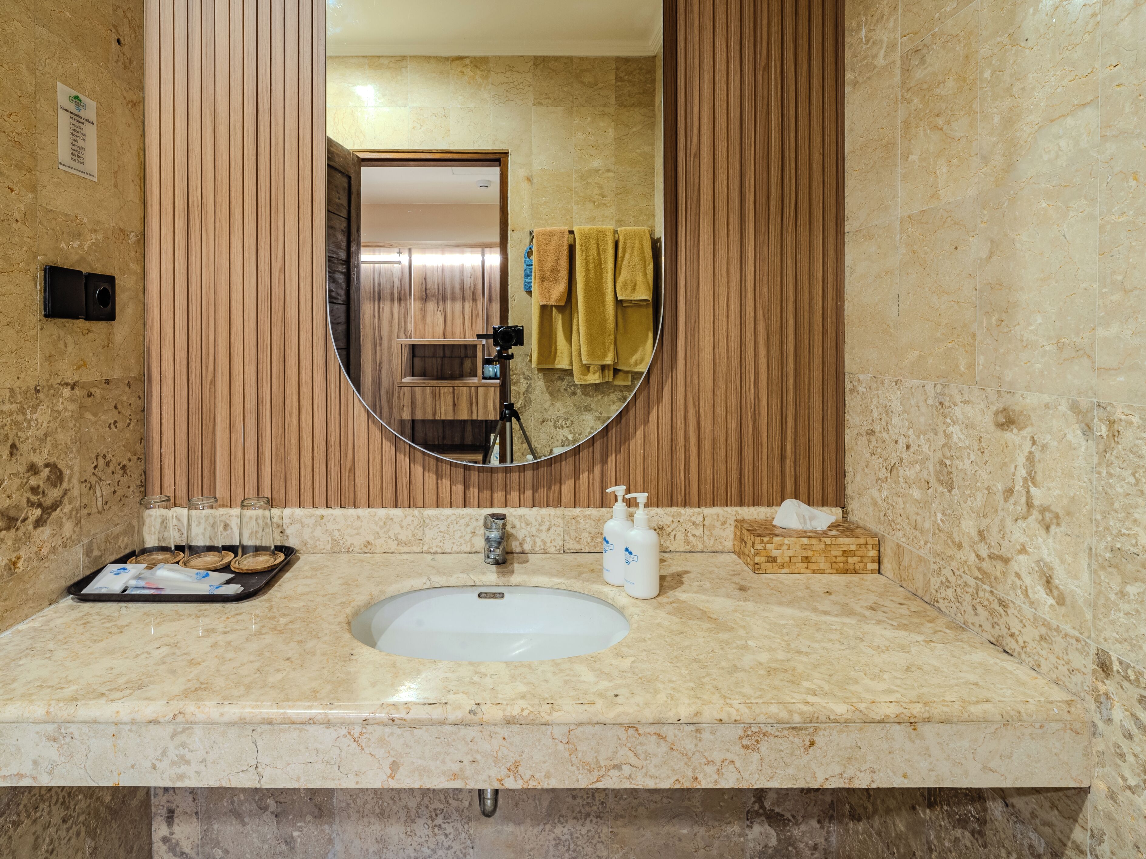 Une salle de bain avec un lavabo en marbre, un lambris en bois, un miroir rond et une étagère en bois.
