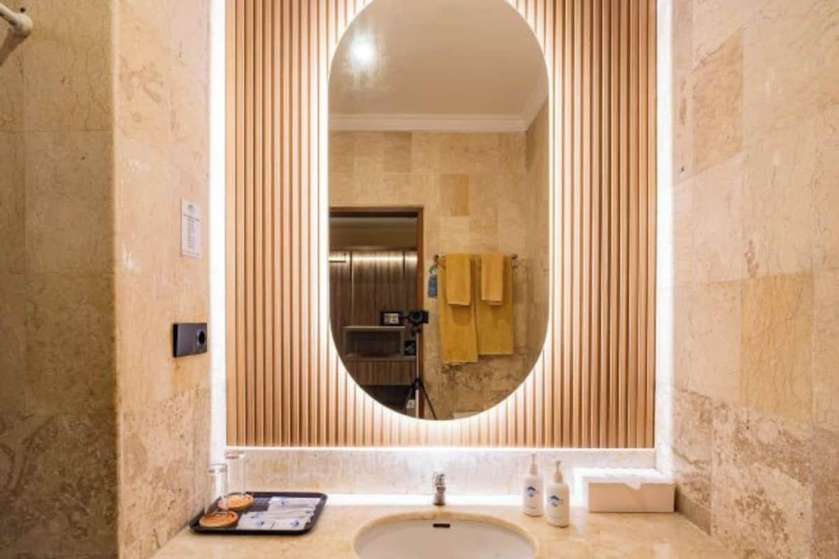 A bathroom with a large oval mirror, a sink, and a tray with toiletries.
