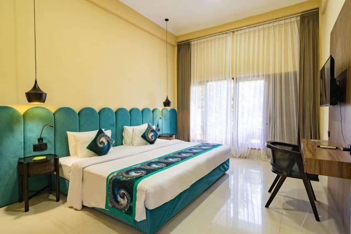 Habitación de hotel con cama, escritorio, silla, televisor y ventana con cortinas.