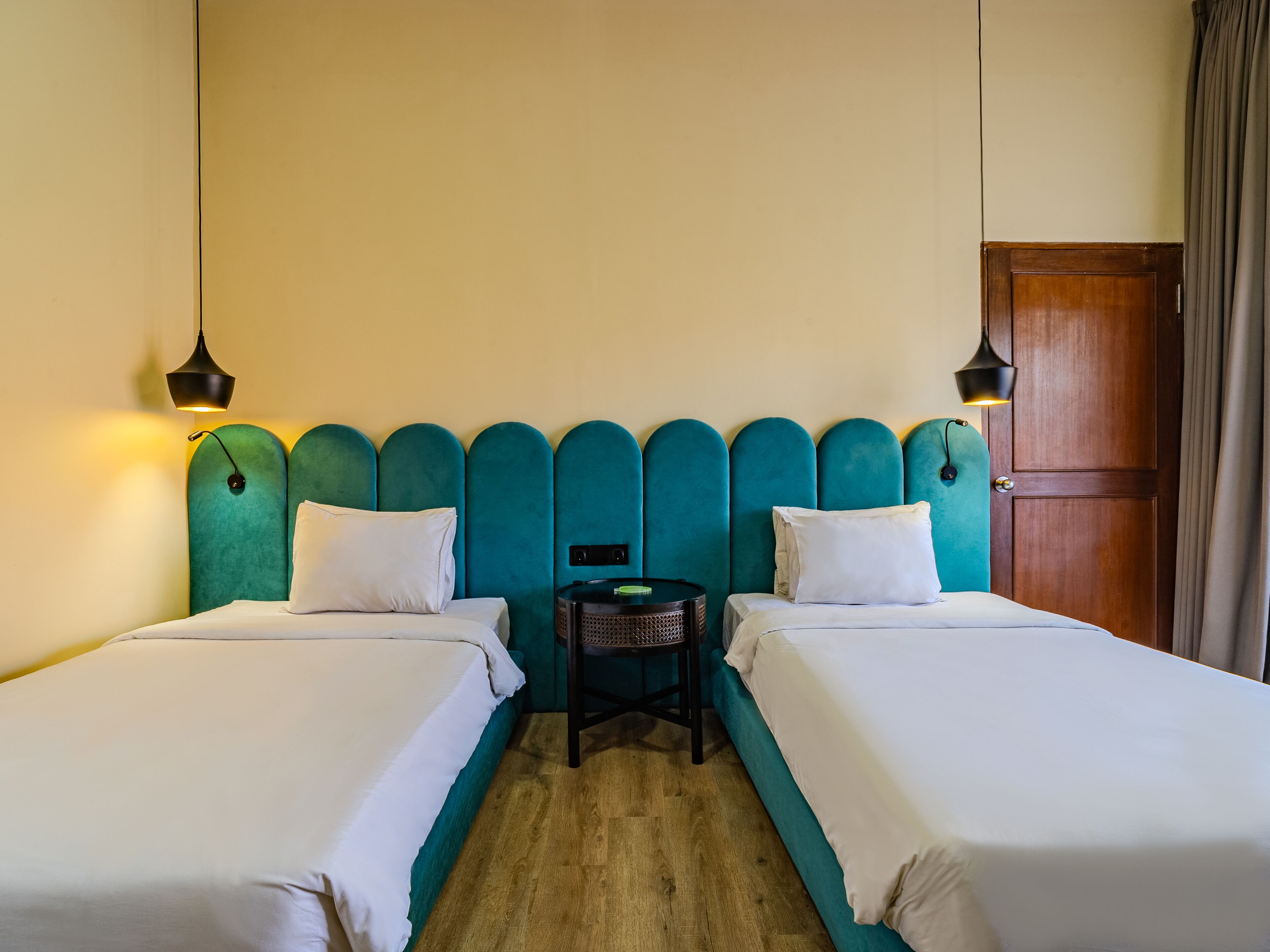 Habitación de hotel con dos camas individuales, una puerta de madera y una pequeña mesa entre las camas.