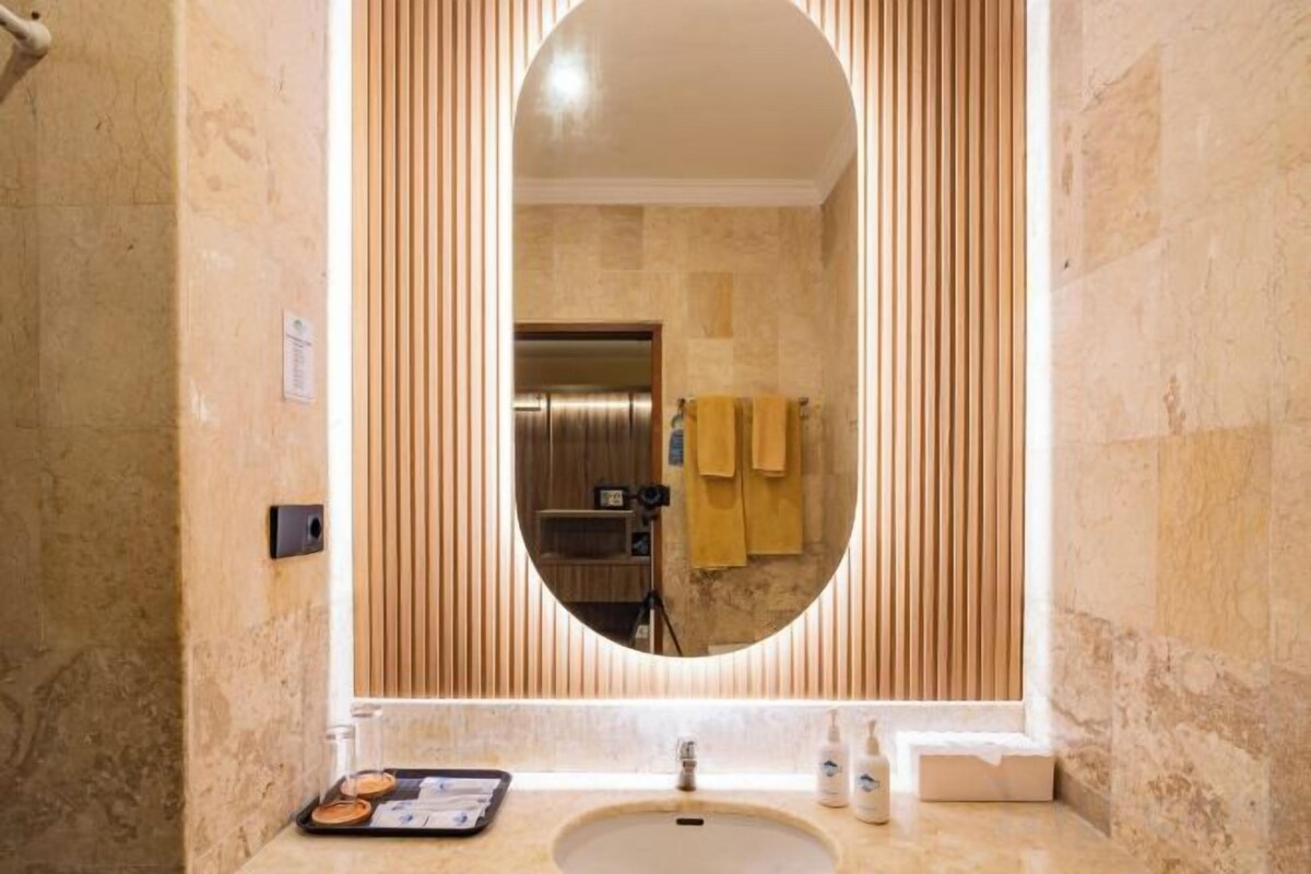 A bathroom with a large oval mirror, a sink, and a towel rack.