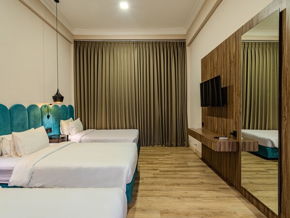 A hotel room with two beds, a wooden floor, a large mirror, and a TV on the wall. - Marine Bay Sanur (Denpasar)