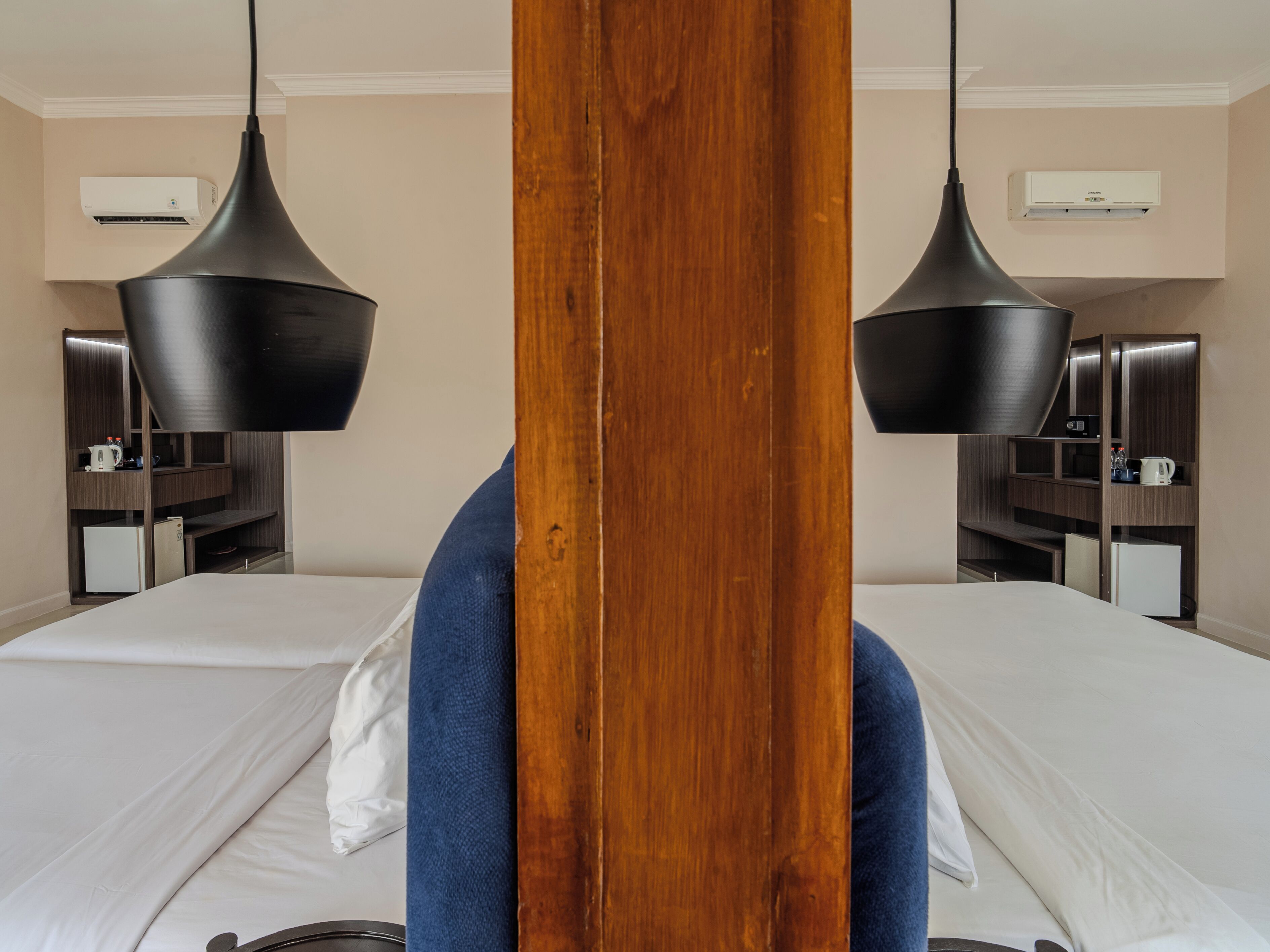 Een hotelkamer met twee bedden, een houten hoofdbord en hanglampen.