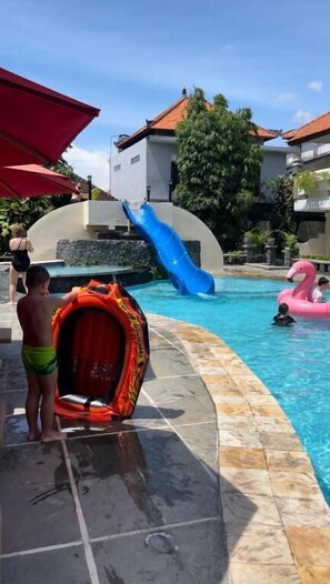 A swimming pool with a slide, a pink flamingo float, and a red tent-like structure. - Marine Bay Sanur (Denpasar)