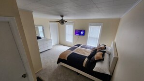 A bedroom with a bed, a dresser, a ceiling fan, a TV, and windows with blinds.
