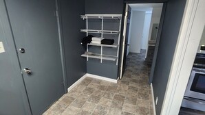 A hallway with a grey door, a white metal shelf unit, and a tiled floor.