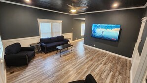 A living room with a dark gray wall, a black sofa, a coffee table, and a TV mounted on the wall displaying a movie.