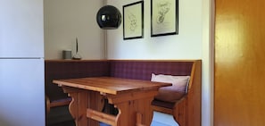Mesa e banco de madeira em um quarto com parede branca, quadros pendurados e luminária.