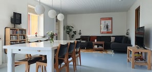 Un salon moderne comprenant une table à manger, des chaises, un canapé, un téléviseur et une bibliothèque.