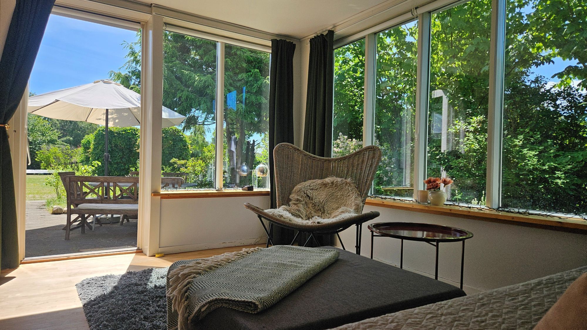 Une pièce avec une grande fenêtre, un fauteuil en osier, une petite table et un canapé.