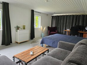 A modern bedroom with a bed, a desk, a chair, a sofa, a dresser, and a window with curtains.