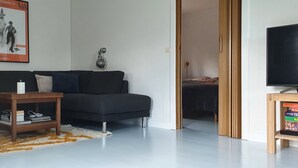 Una sala de estar con un sofá de color oscuro, una mesita de madera, una vela blanca y un cartel en la pared.