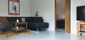 Un salon avec un canapé de couleur sombre, une petite table d’appoint en bois, une bougie blanche et une affiche accrochée au mur.