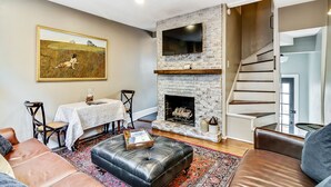 A living room with a fireplace, a dining area, and a staircase. - Cozy & Historic Gem: Free Parking+ Patio -Sleeps 6 (Philadelphia)