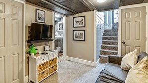 A hallway with a TV, framed pictures, a staircase, and a couch. - Cozy & Historic Gem: Free Parking+ Patio -Sleeps 6 (Philadelphia)