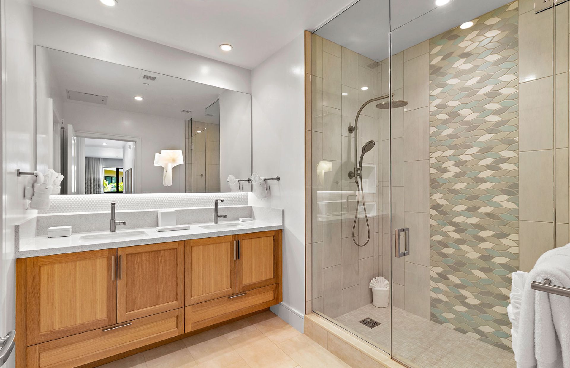 Un baño moderno con ducha envuelta en vidrio, un espejo grande y armarios de madera.