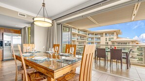 A dining area with a wooden table and chairs, a modern chandelier, and a view of a residential building.