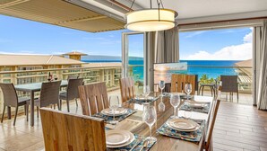 A dining area with a view of the ocean, a large window, and a ceiling fan.