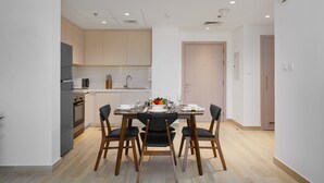 A modern kitchen with wooden cabinets, a dining table set for four, and a microwave. - Maison Privee - Exquisite Apt on Yas Island cls to ALL attractions (Abu Dhabi)