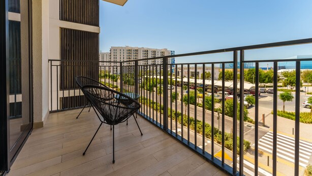 A balcony with a black chair, a view of a cityscape, and a clear sky. - Maison Privee - Exquisite Apt on Yas Island cls to ALL attractions (Abu Dhabi)