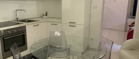 A modern kitchen with white cabinets, stainless steel appliances, and a glass dining table with chairs.