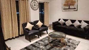 Una sala de estar moderna con un sofá negro, dos sillones, una mesa de centro redonda y un gran reloj de pared.