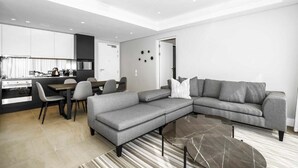 Ein modernes Wohnzimmer mit einem grauen Ecksofa, einem Essbereich mit Tisch und Stühlen sowie einer Küche im Hintergrund.