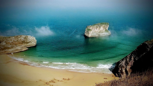 Una platja amb aigua turquesa cristal·lina, sorra daurada i formacions rocoses.