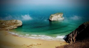 Ein Strand mit klarem türkisblauem Wasser, sandigem Ufer und Felsformationen.