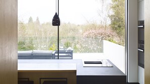A modern kitchen with a large window, a hanging light fixture, and built-in appliances.