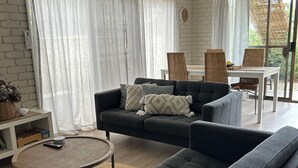 Un salon moderne avec un canapé gris foncé, une table basse ronde et un coin repas doté de chaises en osier.